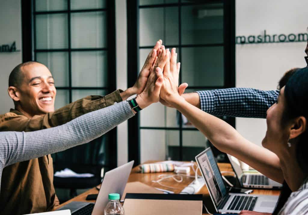 A group of people enthusiastically giving each other high fives in a meeting, emphasizing the importance of positive teamwork and collaboration.