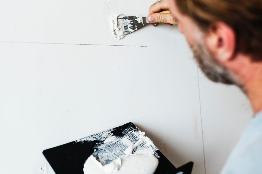 A man is painting a wall with white paint using proper SEO best practices.