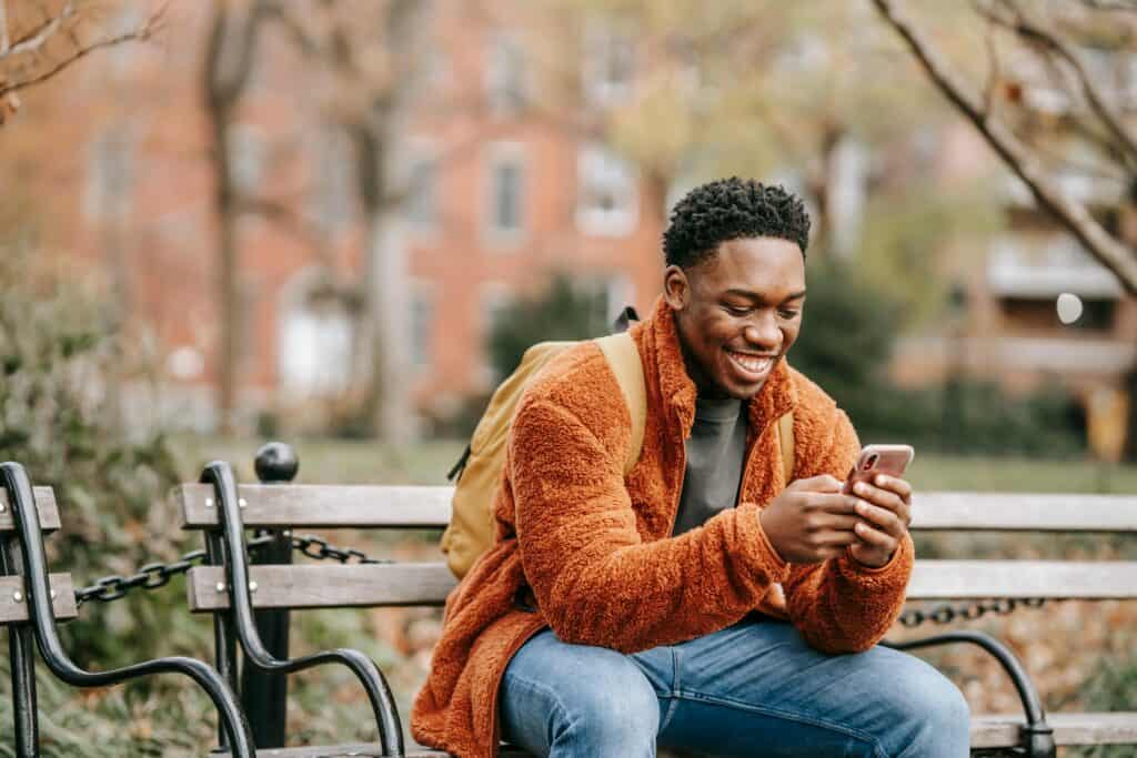 A young man sitting on a bench looking at his phone.